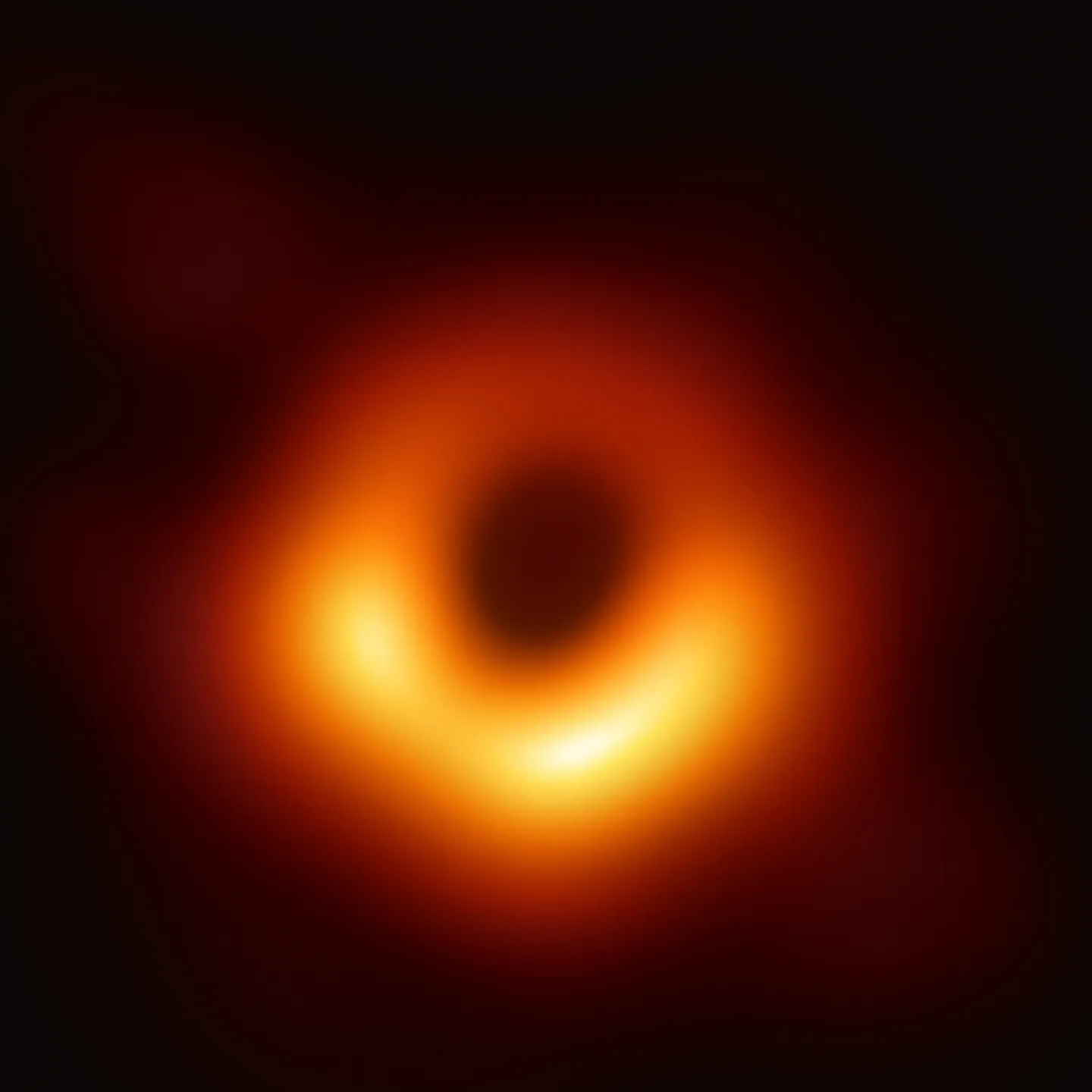 A blurred ring of orange and yellow light around a dark round center on a black background; the ring is brightest along its lower half.